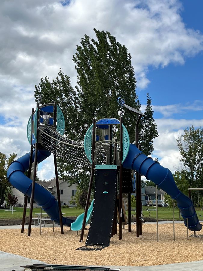 Blue and teal multi-level playground with tube slide, rope climber and Nido Spinner.