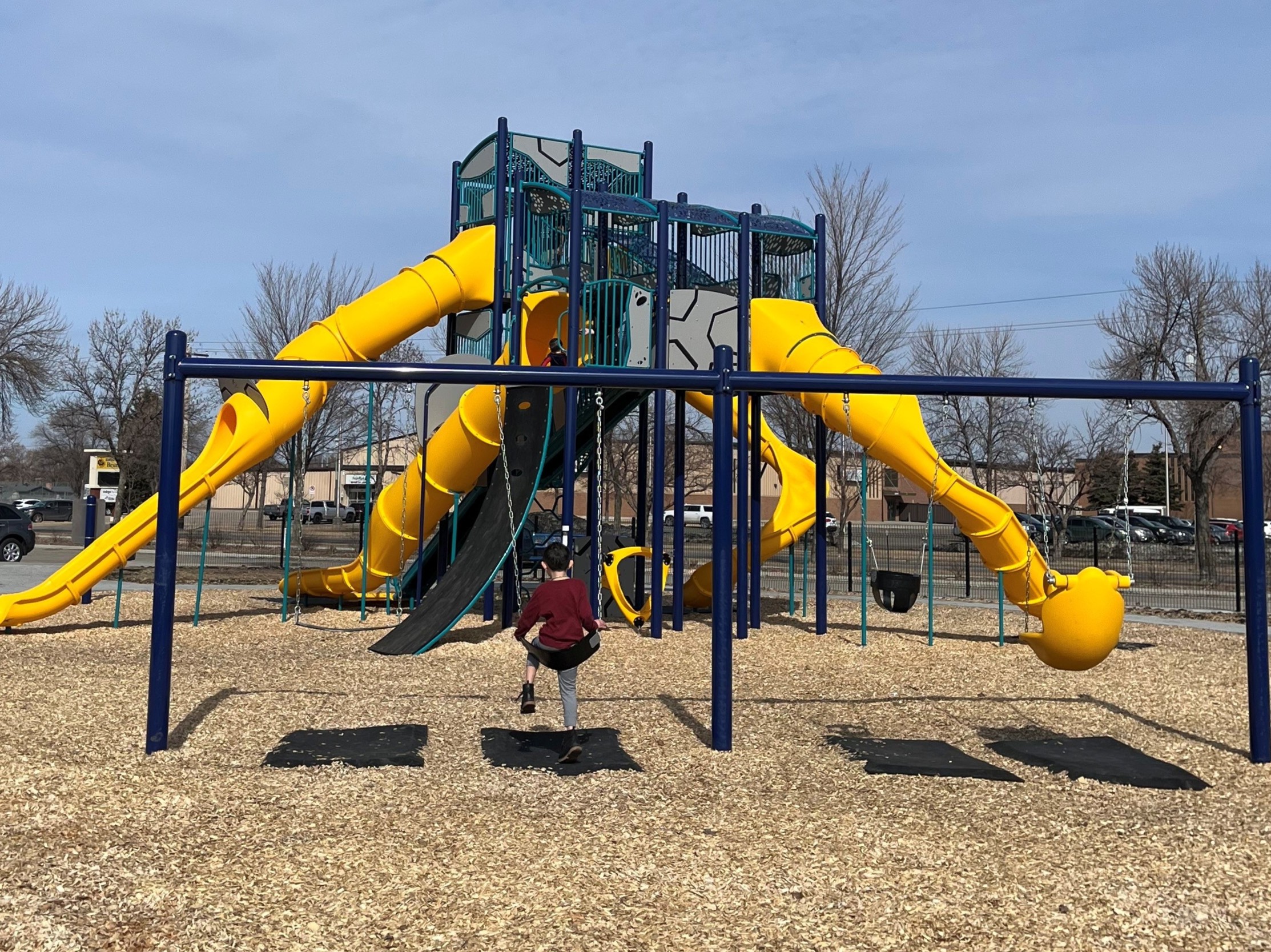 Navy swing structure with two swings, one baby swing and yellow adaptive swing.  Play structure located behind swings.